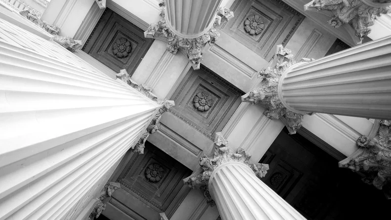 A black and white image of four Corinthian columns holding up a coffered ceiling.